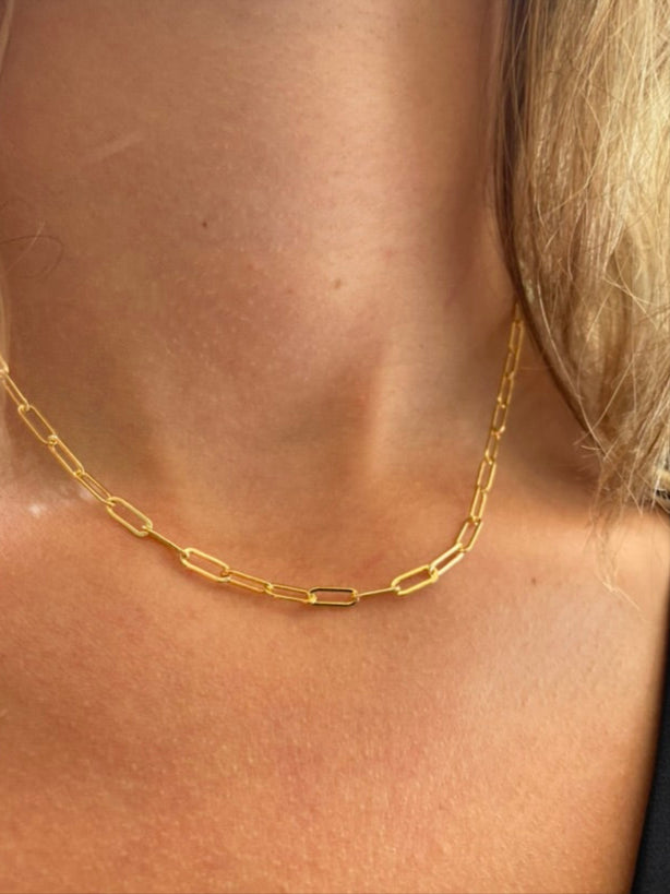 A gold paperclip chain necklace worn on a model showing the chain detail around the neck