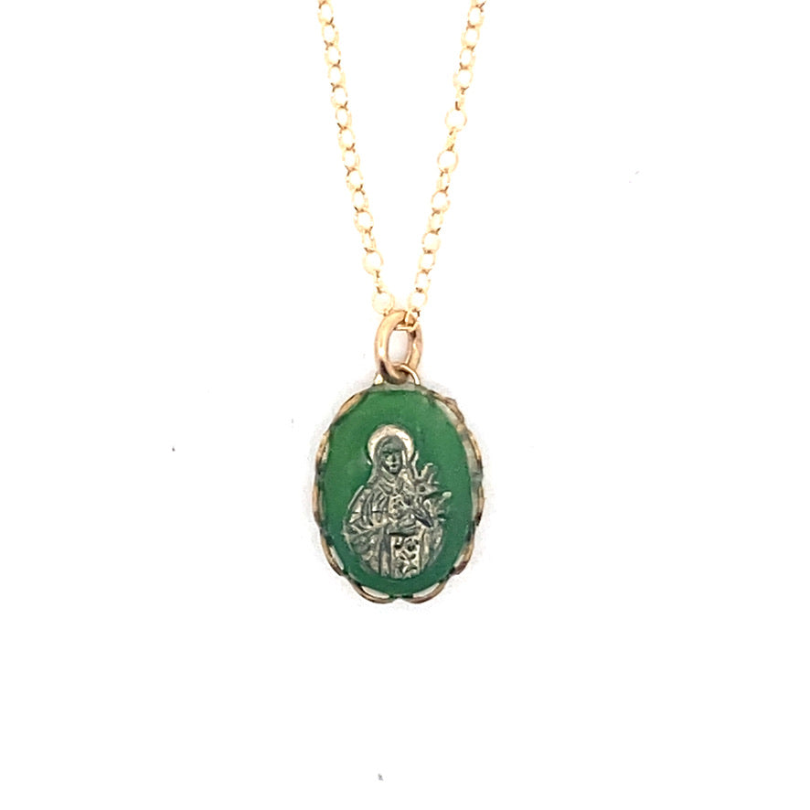 Close-up of a vintage emerald green Virgin Mary cameo pendant with gold overlay on a delicate gold chain against a white background