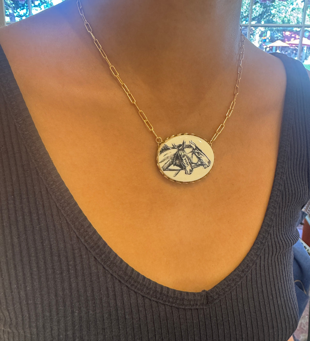 Gold necklace with a circular pendant worn by a person in a dark top.