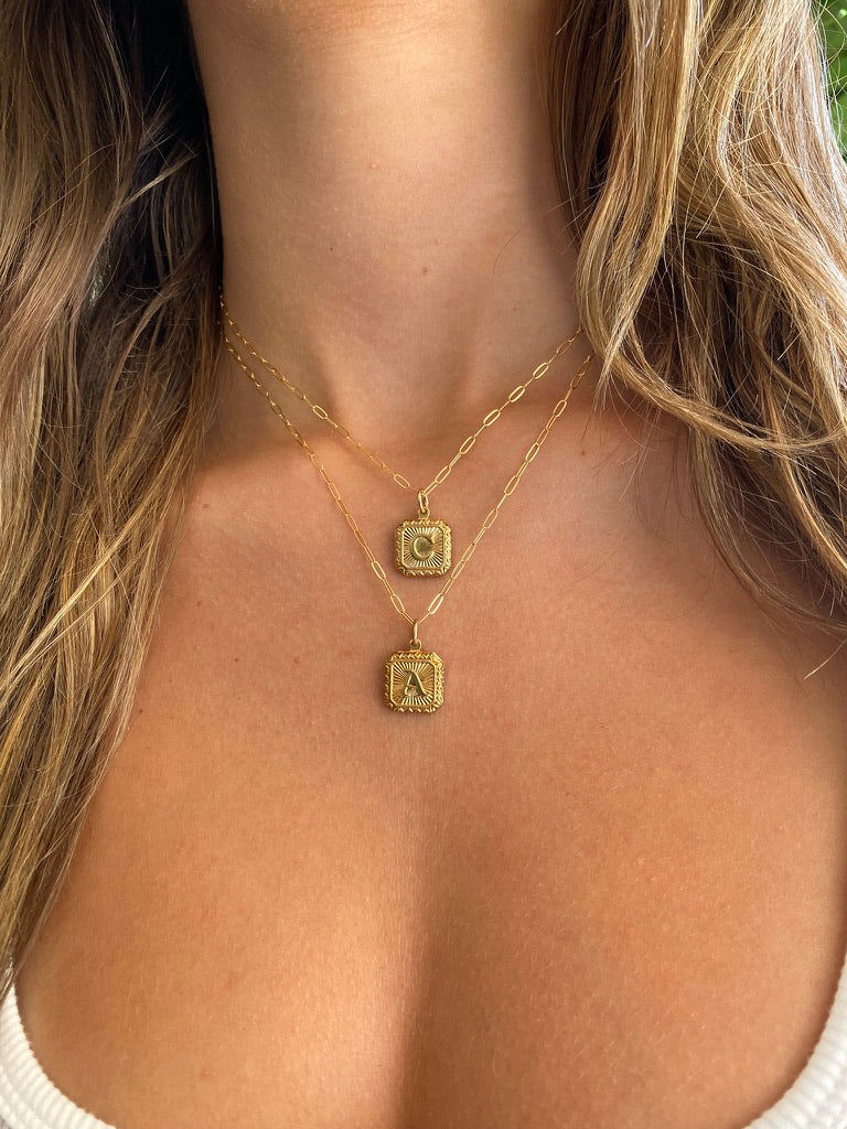 Gold necklaces with square pendants on a person's neck