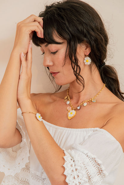 Woman wearing a gold necklace with floral pendants and matching earrings against a neutral background.