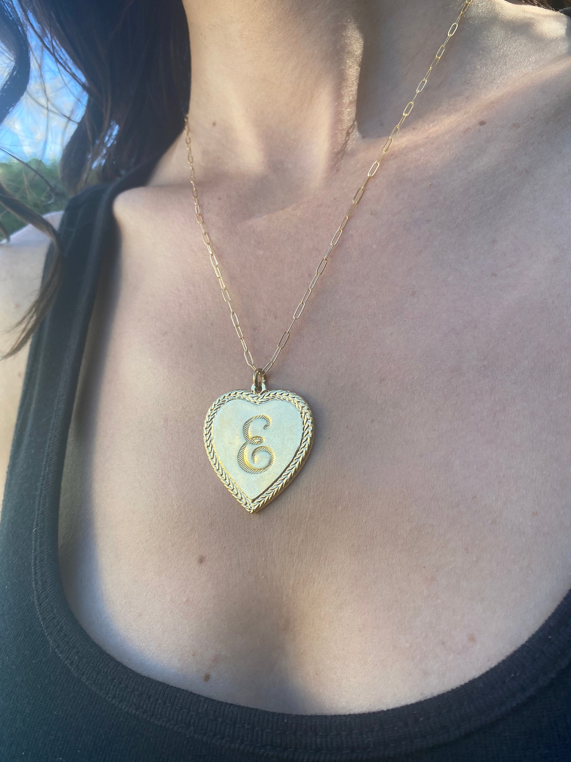 Gold heart pendant necklace with rope twisted border and letter E initial on a mint green enamel background worn on a model on a gold paperclip chain close-up lifestyle photo