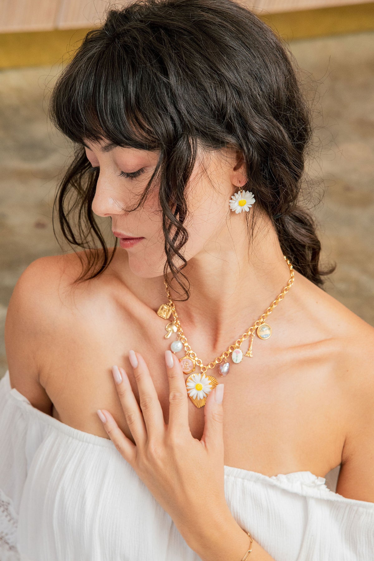 Woman wearing a gold necklace with floral earrings against a neutral background
