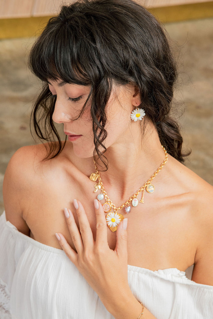 Woman wearing a gold necklace with floral earrings against a neutral background