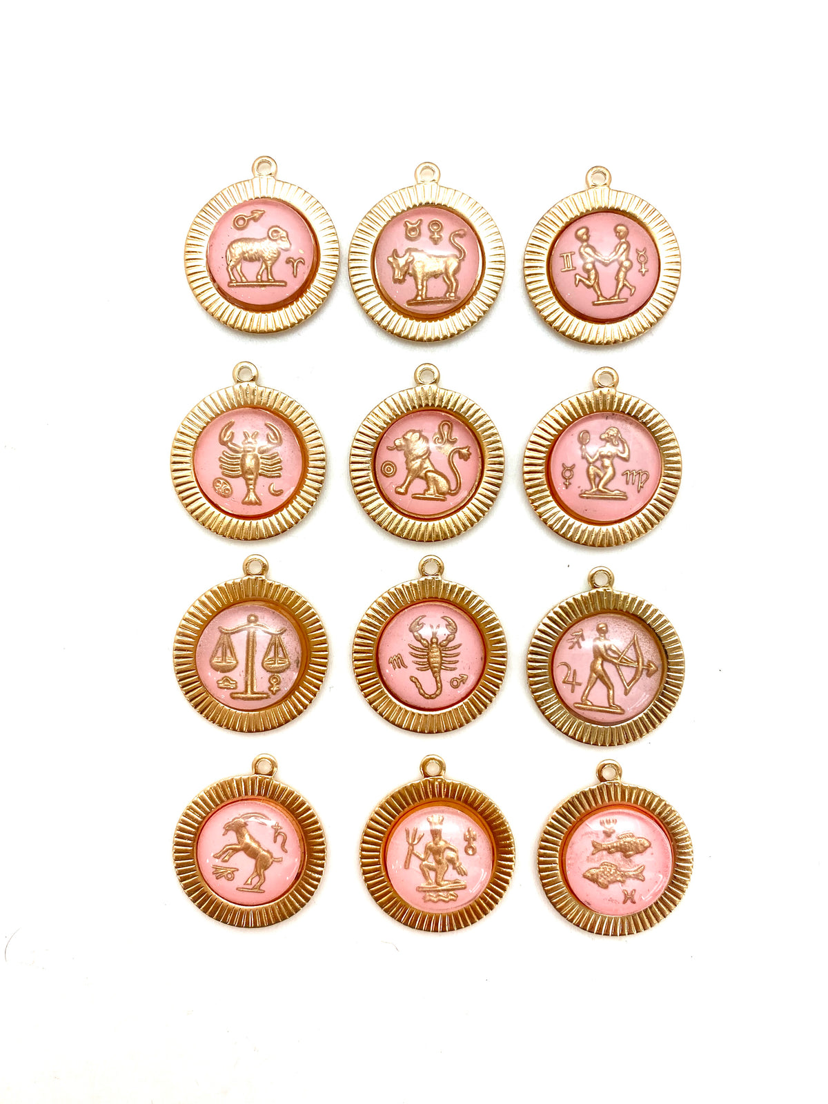 Collection of twelve gold round sunburst pendant charms with pink vintage glass zodiac intaglio cameos featuring all twelve zodiac signs arranged in a grid on a white background