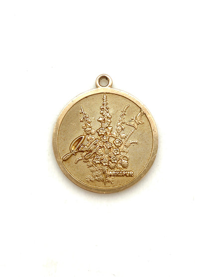 Gold embossed July larkspur birth month flower coin pendant charm on a white background
