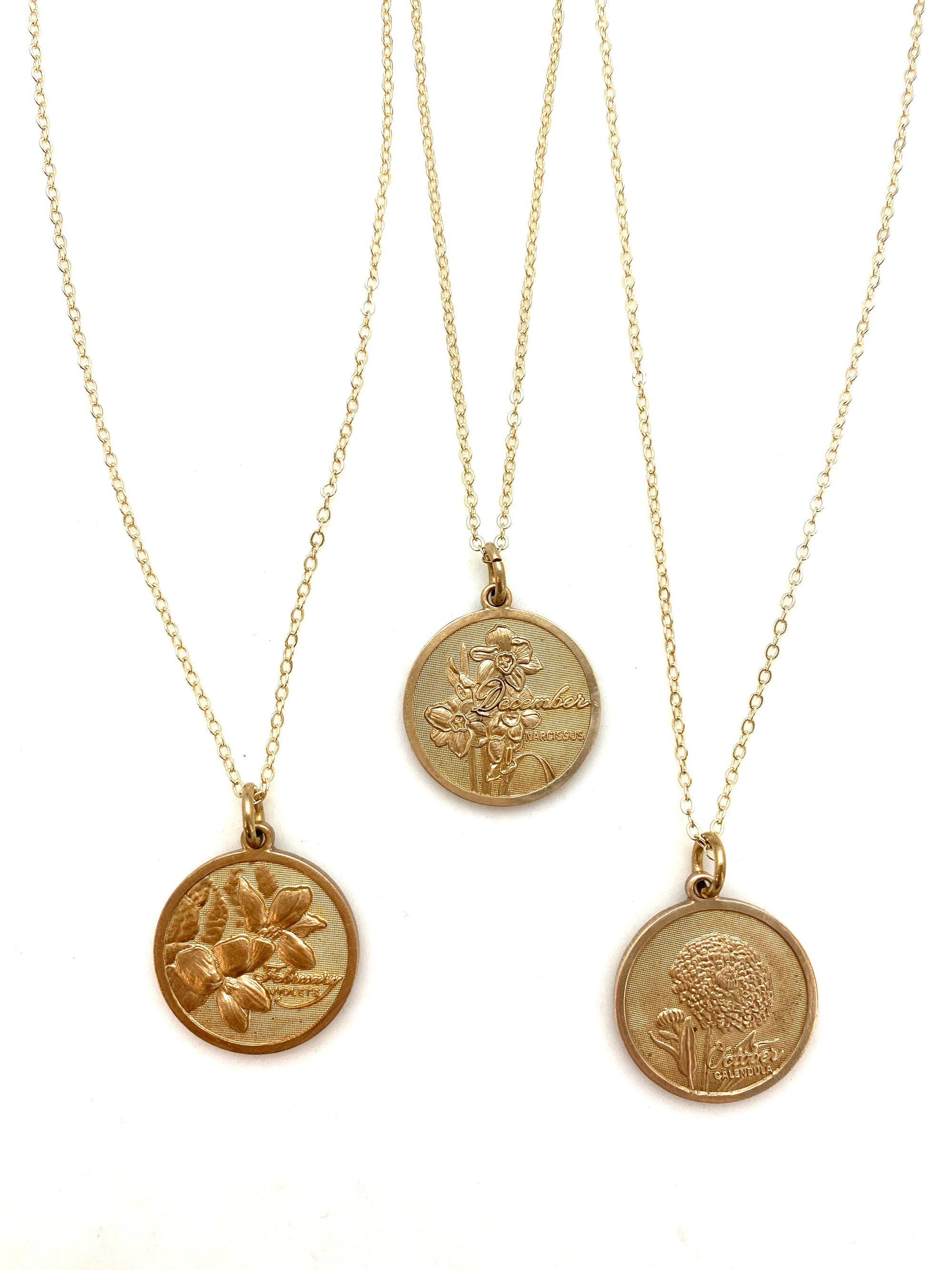 Three gold embossed birth month flower coin pendant necklaces on delicate gold chains displayed on a white background