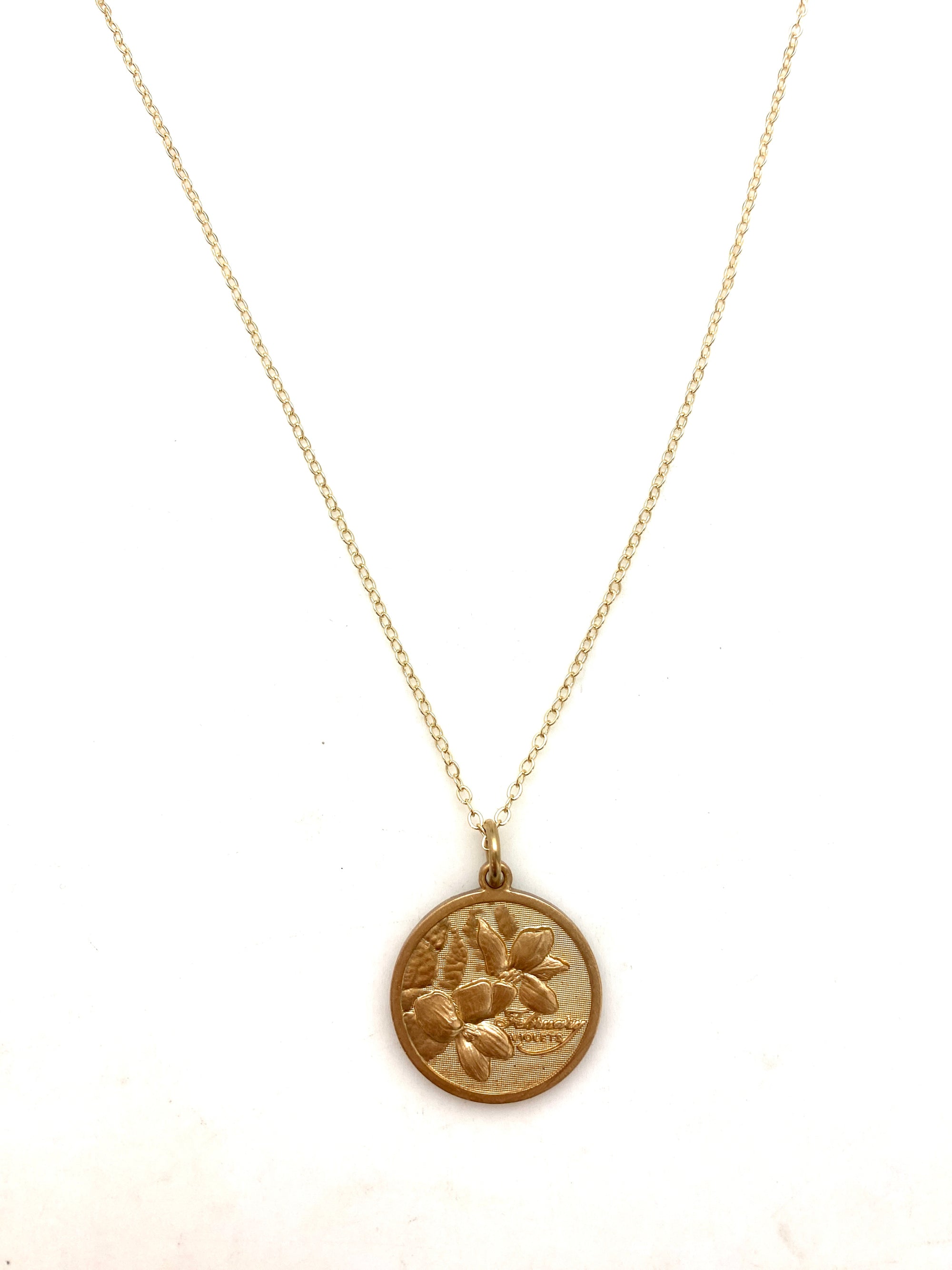 Gold embossed February violet birth month flower coin pendant necklace on a delicate gold chain on a white background