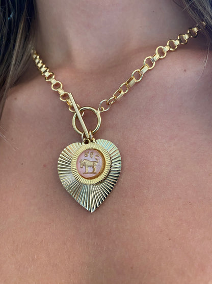 Gold and green patina heart-shaped sunburst pendant necklace with a pink vintage glass Taurus bull intaglio cameo on a gold rolo chain with toggle clasp worn on a model close-up