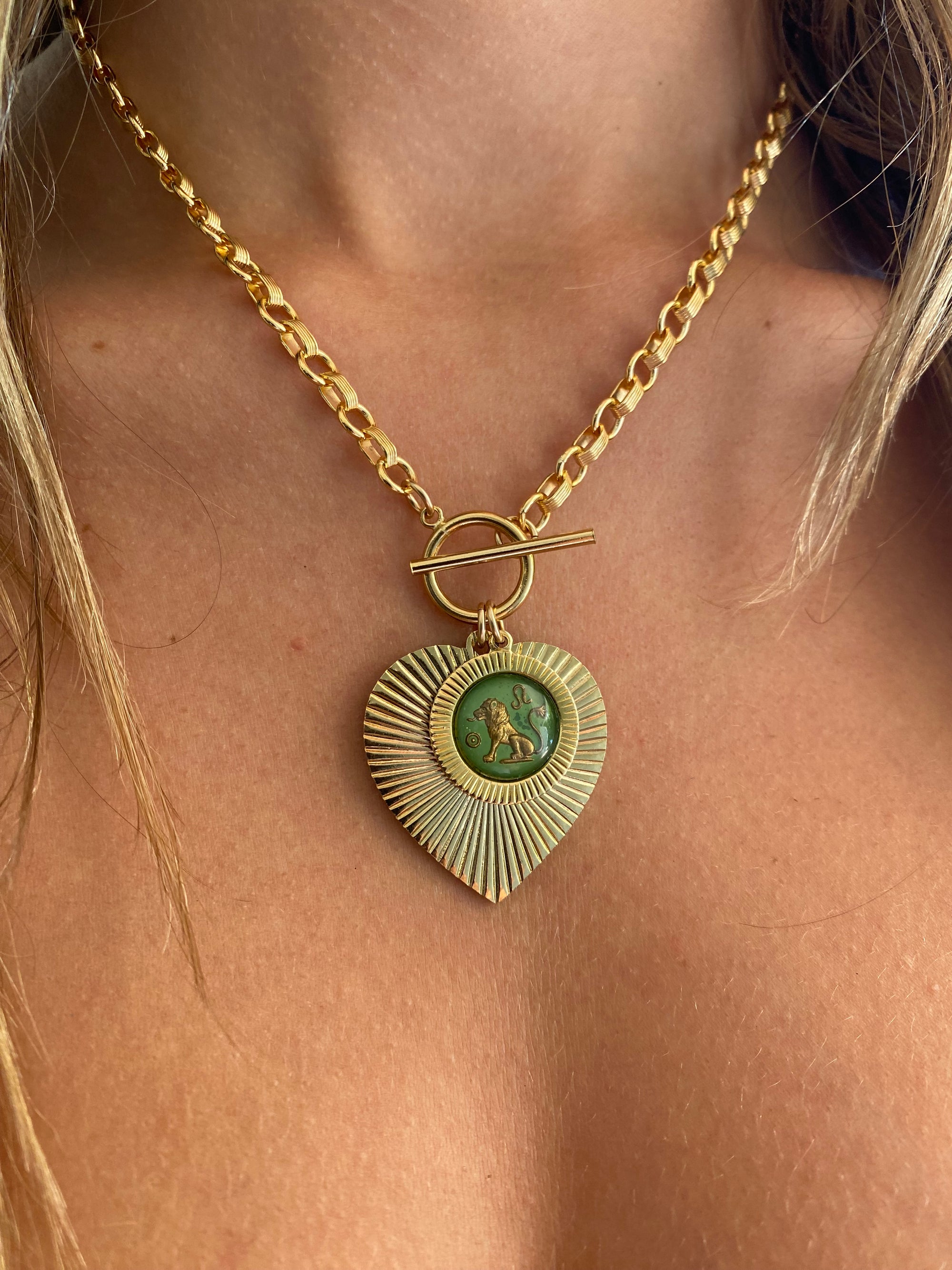 Gold and green patina heart-shaped sunburst pendant necklace with a green vintage glass Leo lion intaglio cameo on a gold rolo chain with toggle clasp worn on a model close-up