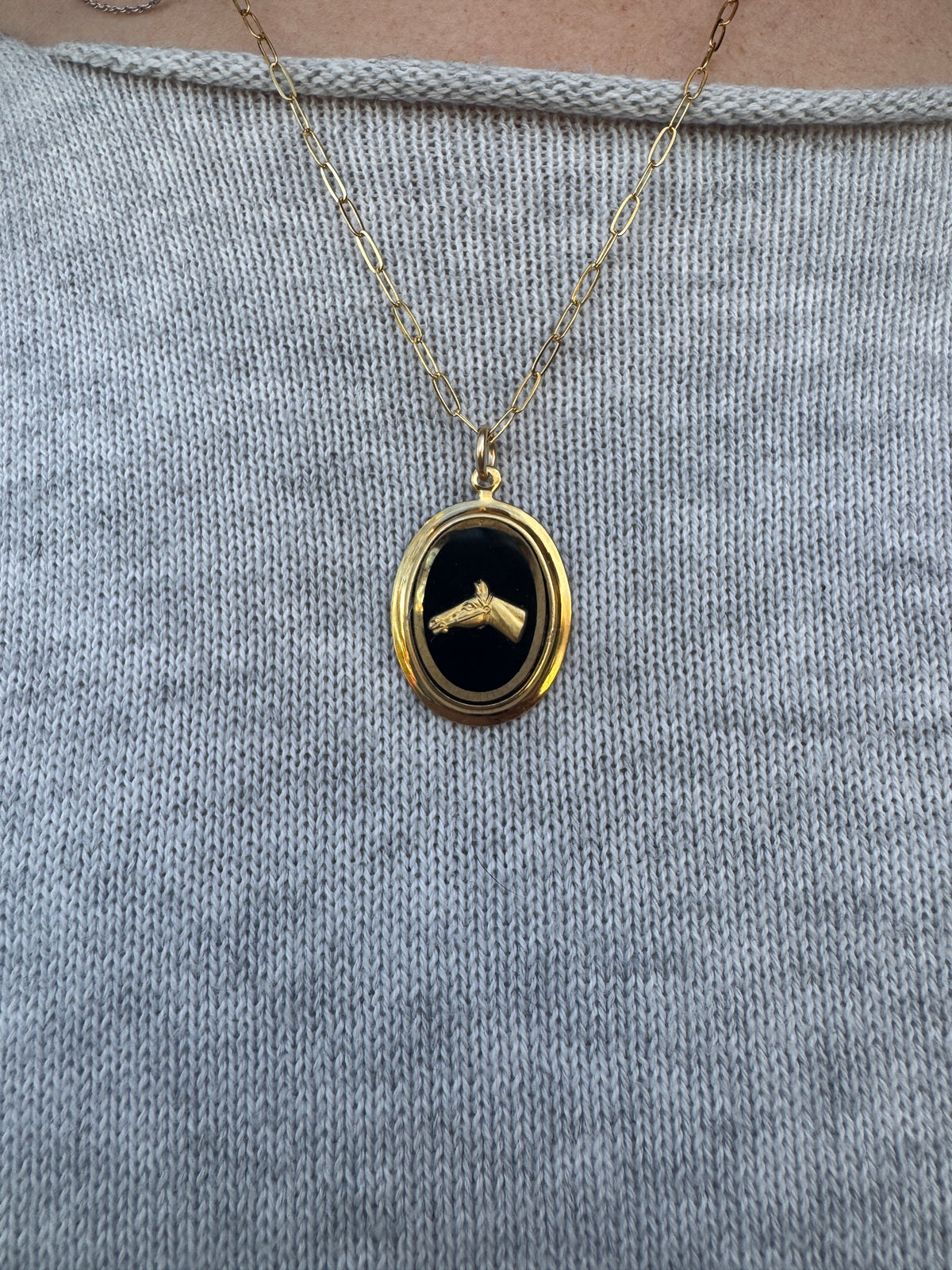 Gold necklace with a black pendant on a textured gray surface