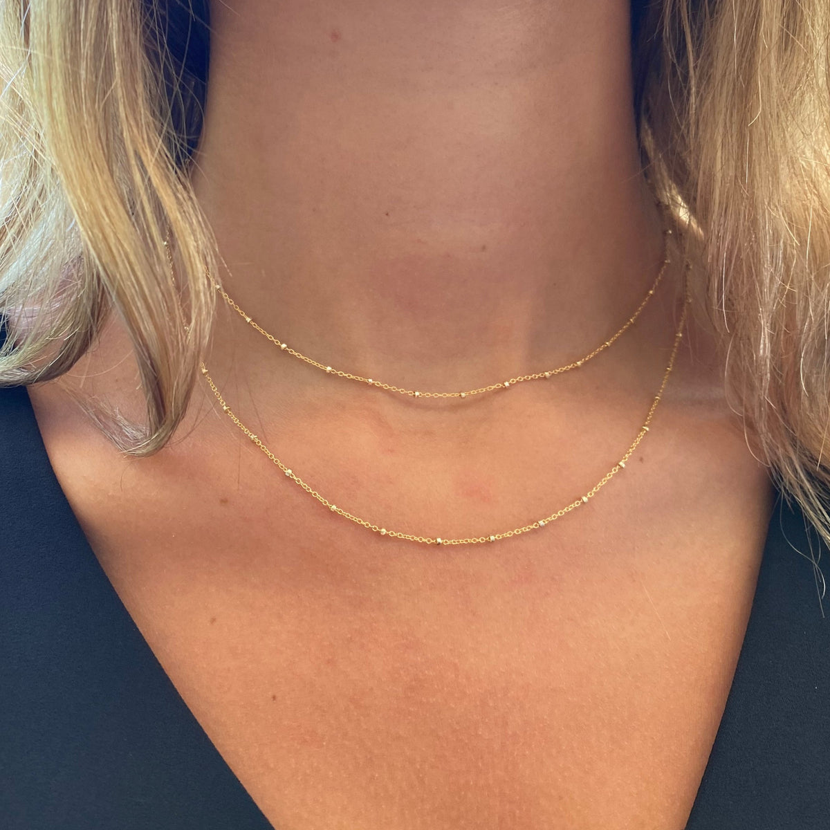 Layered gold satellite beaded chain necklaces worn on a model showing two delicate chains at different lengths against the neckline
