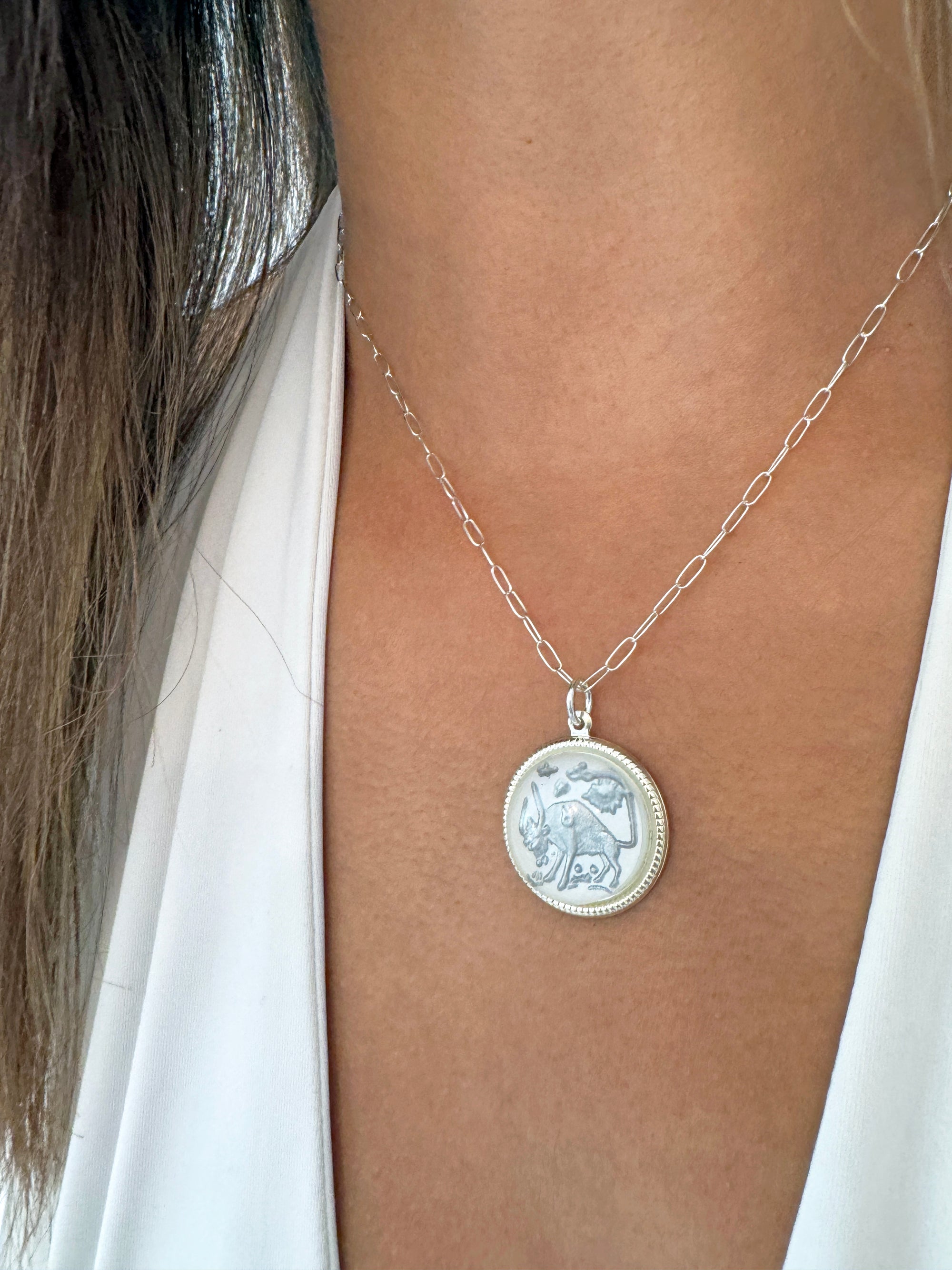 Silver round Taurus zodiac coin pendant with bull design on a silver paperclip chain worn on a model in a white top