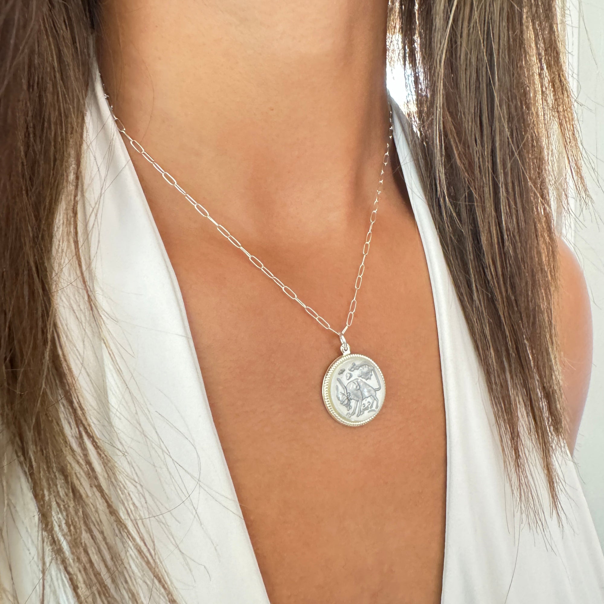 Silver round Taurus zodiac coin pendant with bull design on a silver paperclip chain worn on a model in a white top with wide angle view