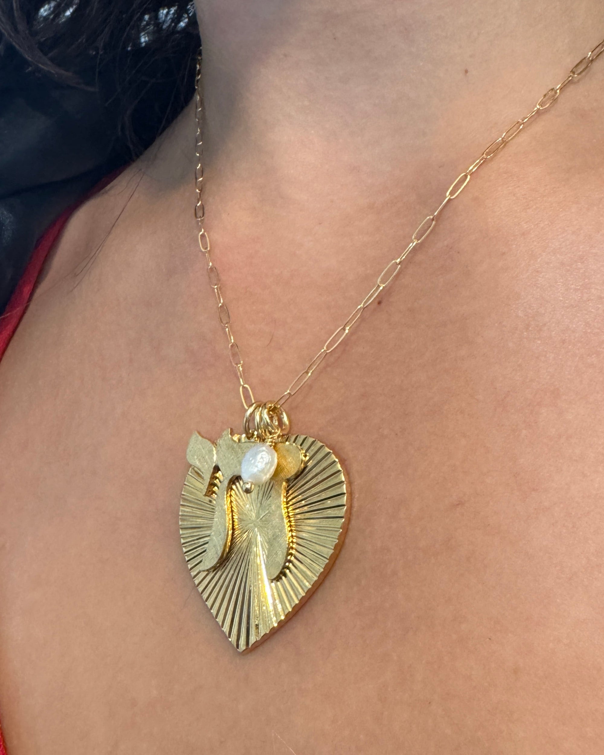 Gold ribbed heart-shaped pendant showing the back with starburst pattern and pearl charm on a gold paperclip chain worn on a model