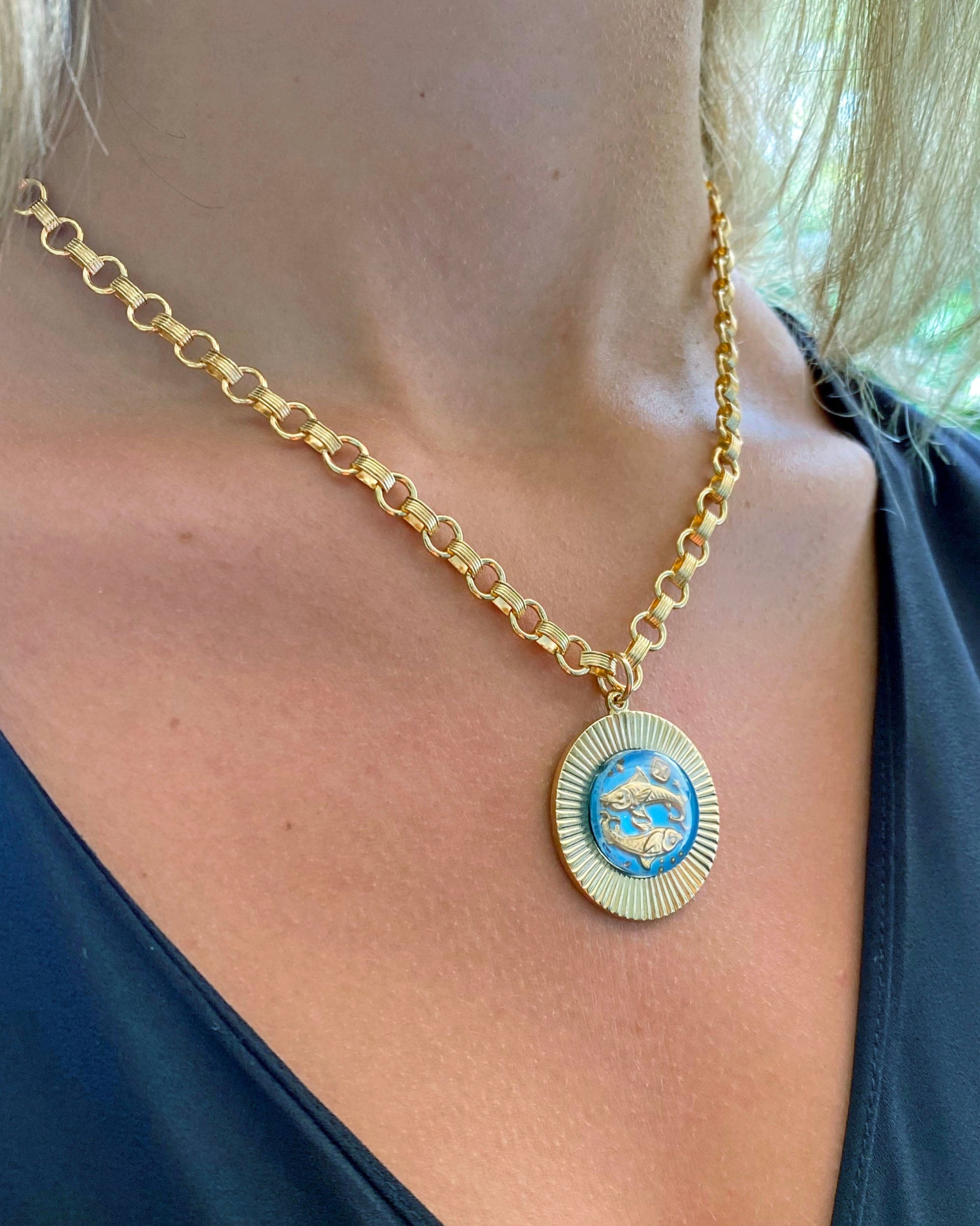 A person wearing a vintage large glass zodiac sign necklace on a gold fill heavy cable chain.