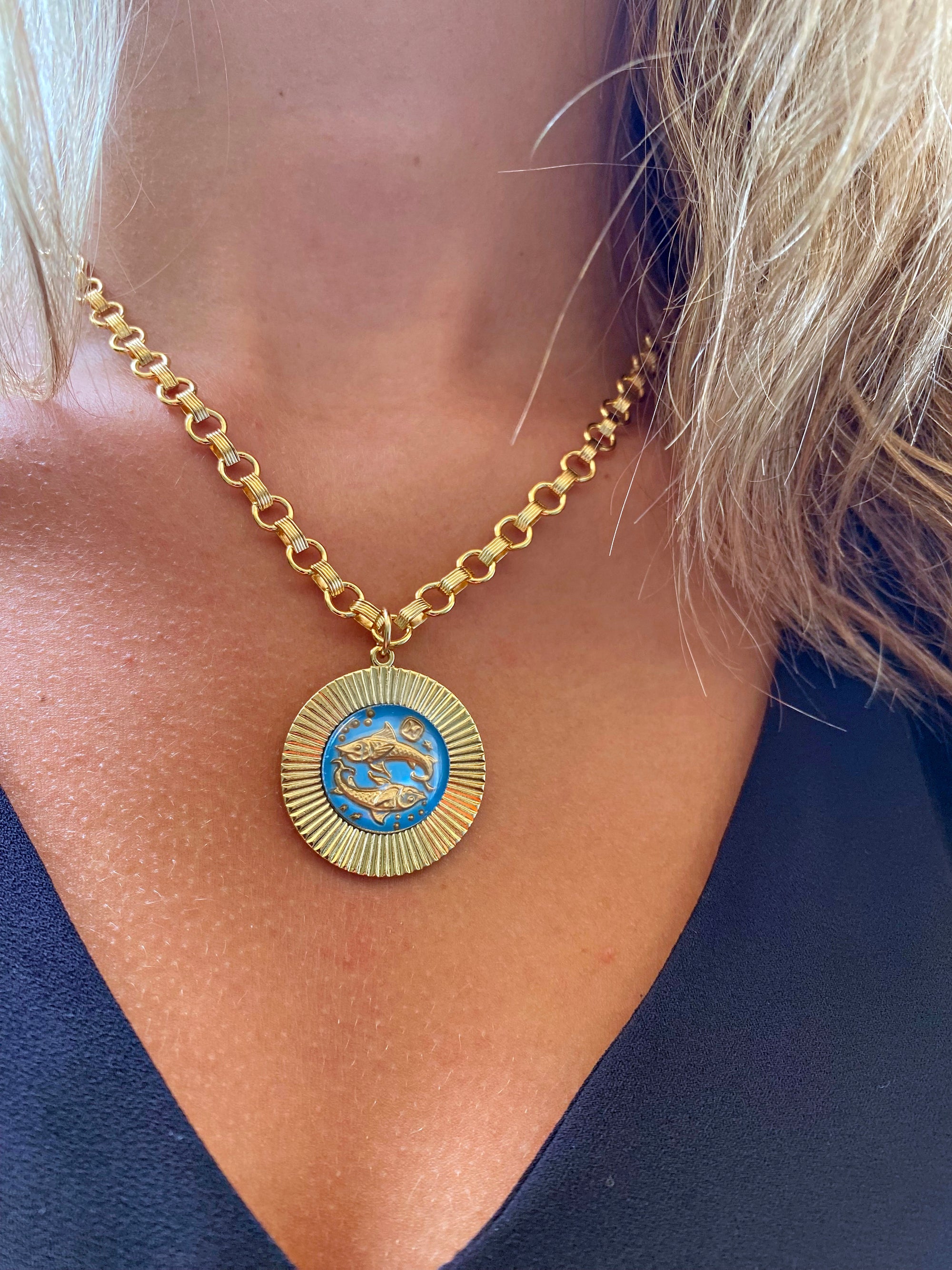 A vintage large glass Pisces zodiac sign necklace with a gold-plated sunburst pendant on a heavy cable chain, displayed on a person's neck