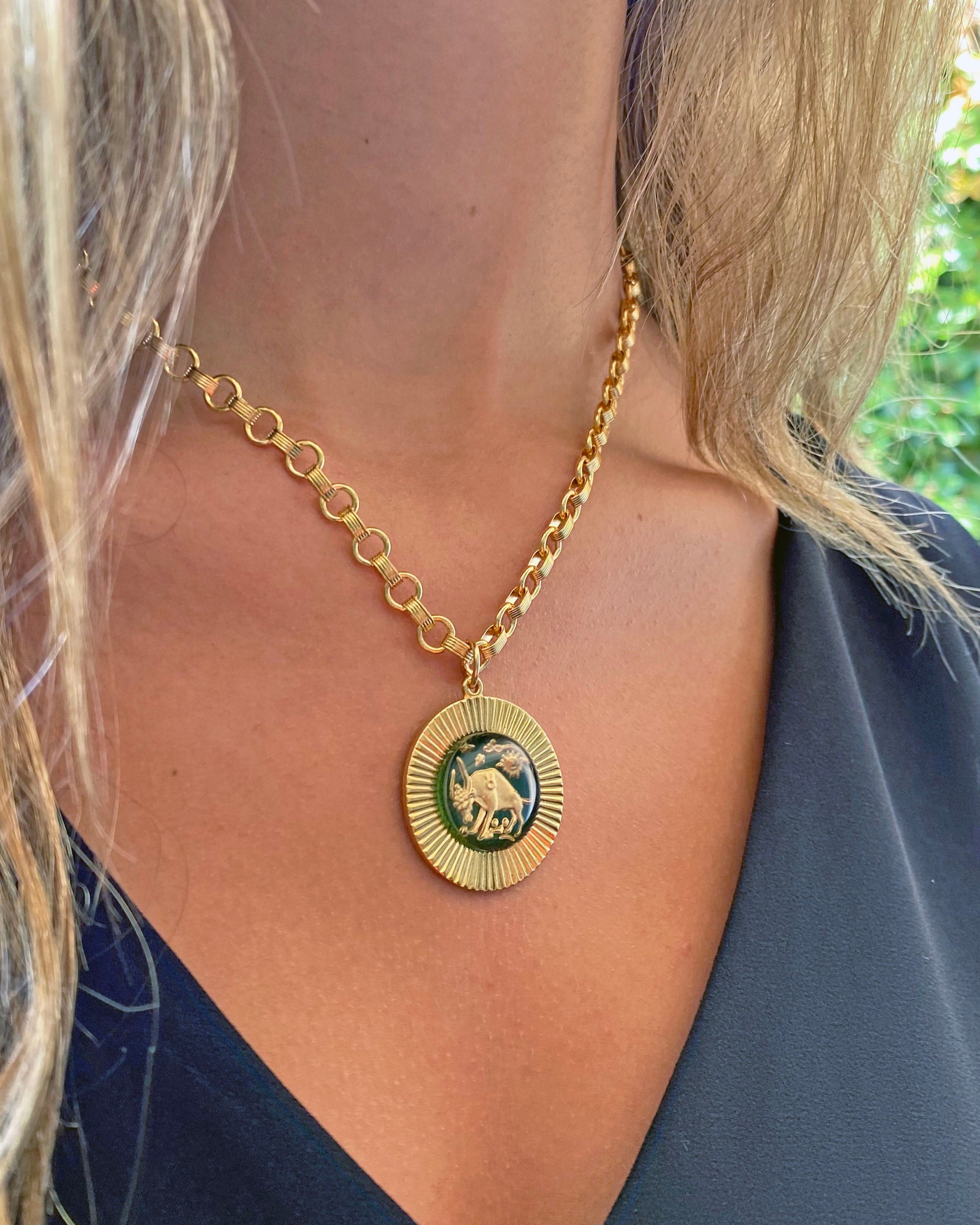 A vintage large glass Taurus zodiac sign necklace with a gold-plated sunburst pendant on a heavy cable chain, displayed on a person's neck