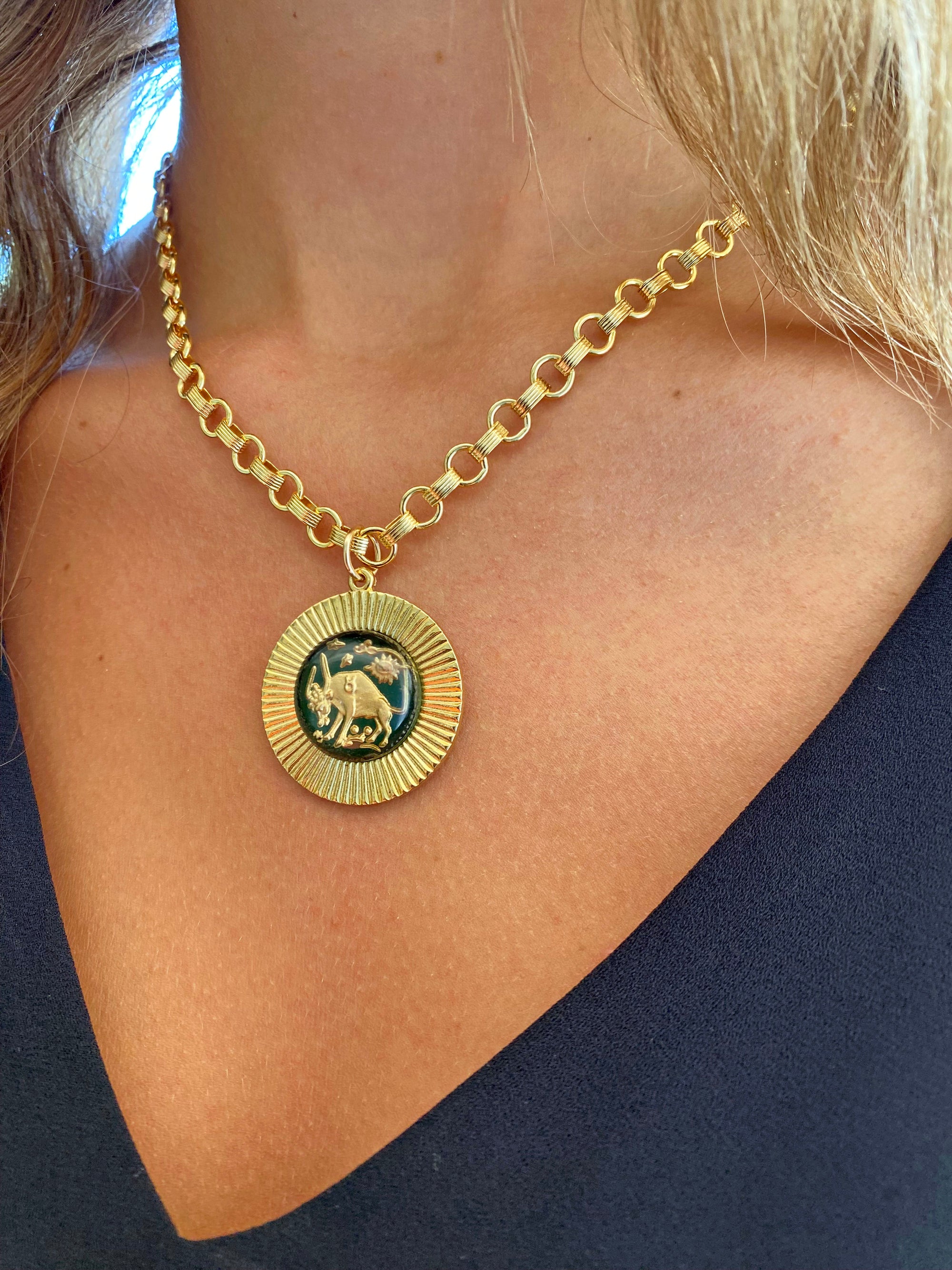 A vintage large glass Taurus zodiac sign necklace with a gold-plated sunburst pendant on a heavy cable chain, displayed on a person's neck