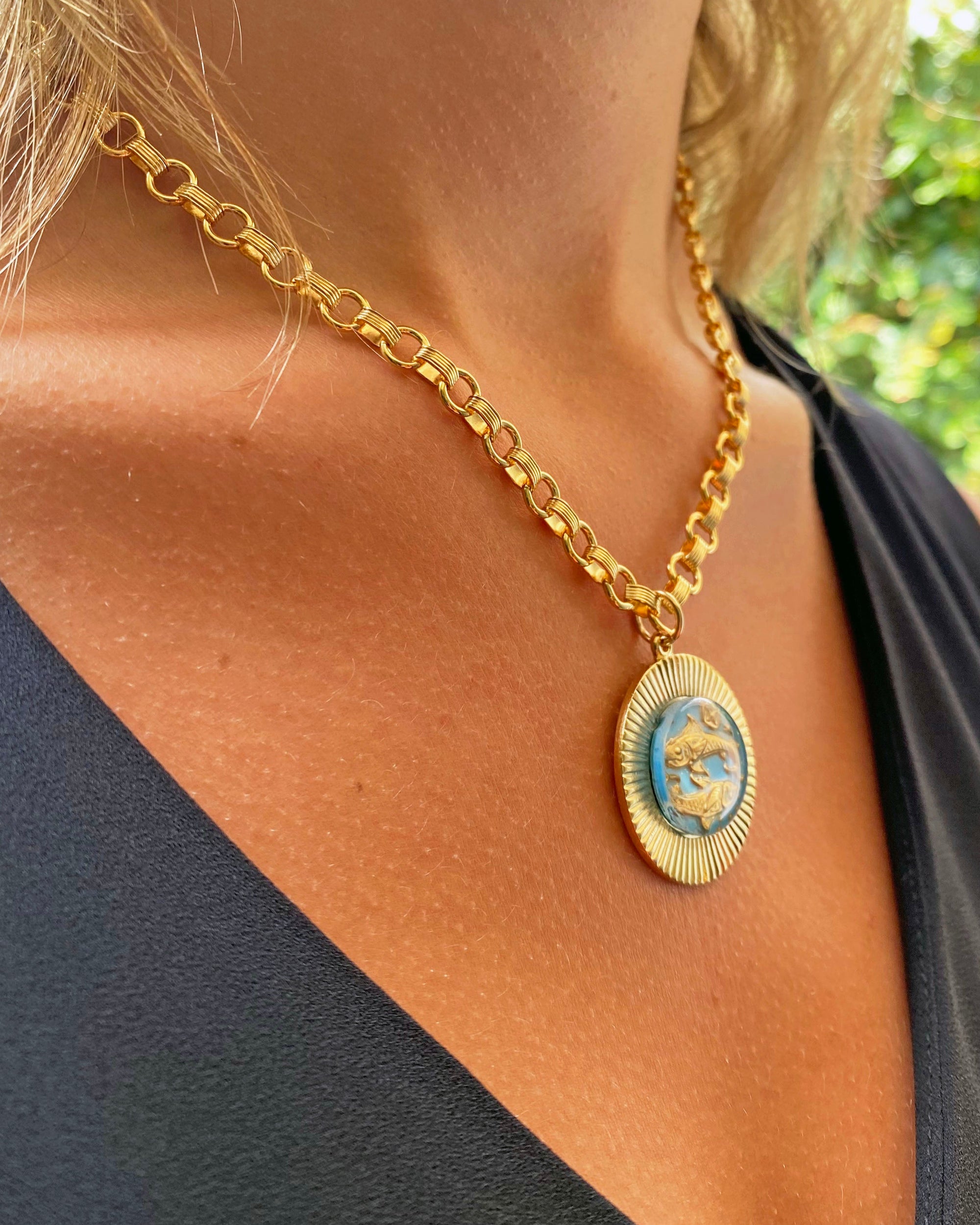 Close-up profile view of a vintage large glass Pisces zodiac sign pendant with blue enamel and gold fish design on a heavy cable chain necklace