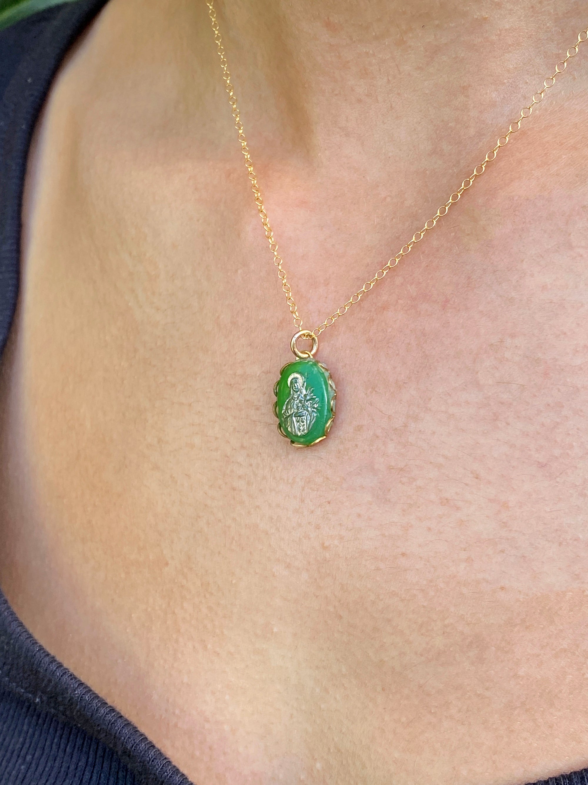 A vintage emerald green Virgin Mary cameo pendant necklace with gold overlay on a delicate gold chain, worn on a person's chest