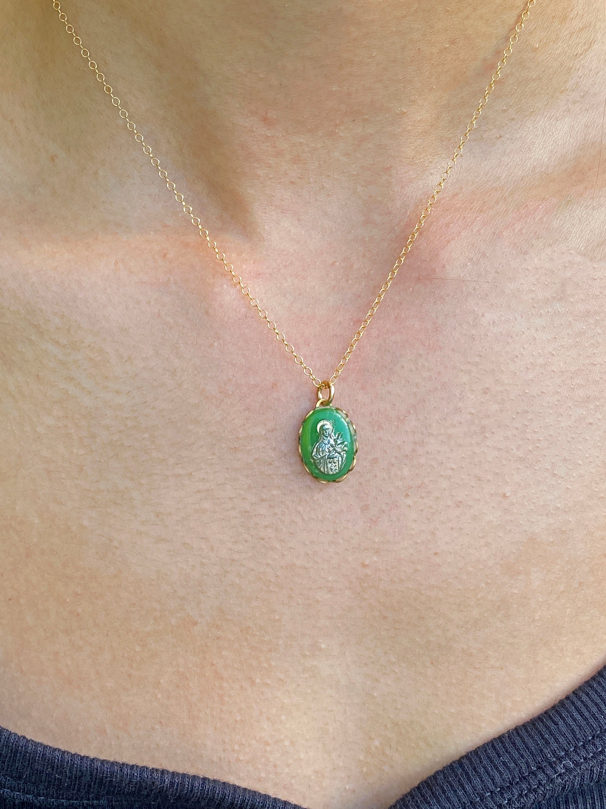 A vintage emerald green Virgin Mary cameo pendant necklace with gold overlay on a delicate gold chain, displayed on a person's neck