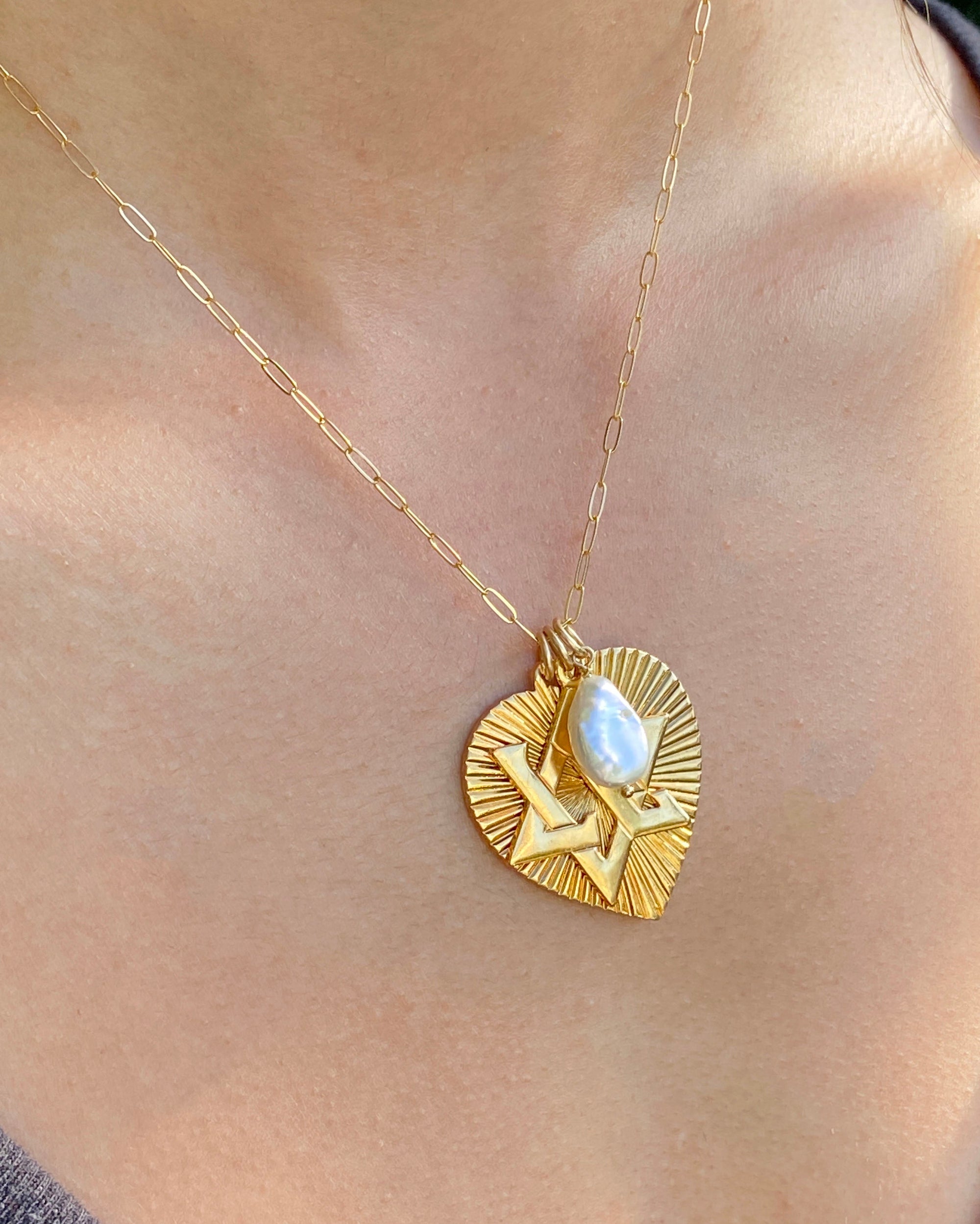 A gold-plated necklace featuring a ribbed heart with a Star of David charm and a large freshwater pearl pendant, displayed on a person's neck.