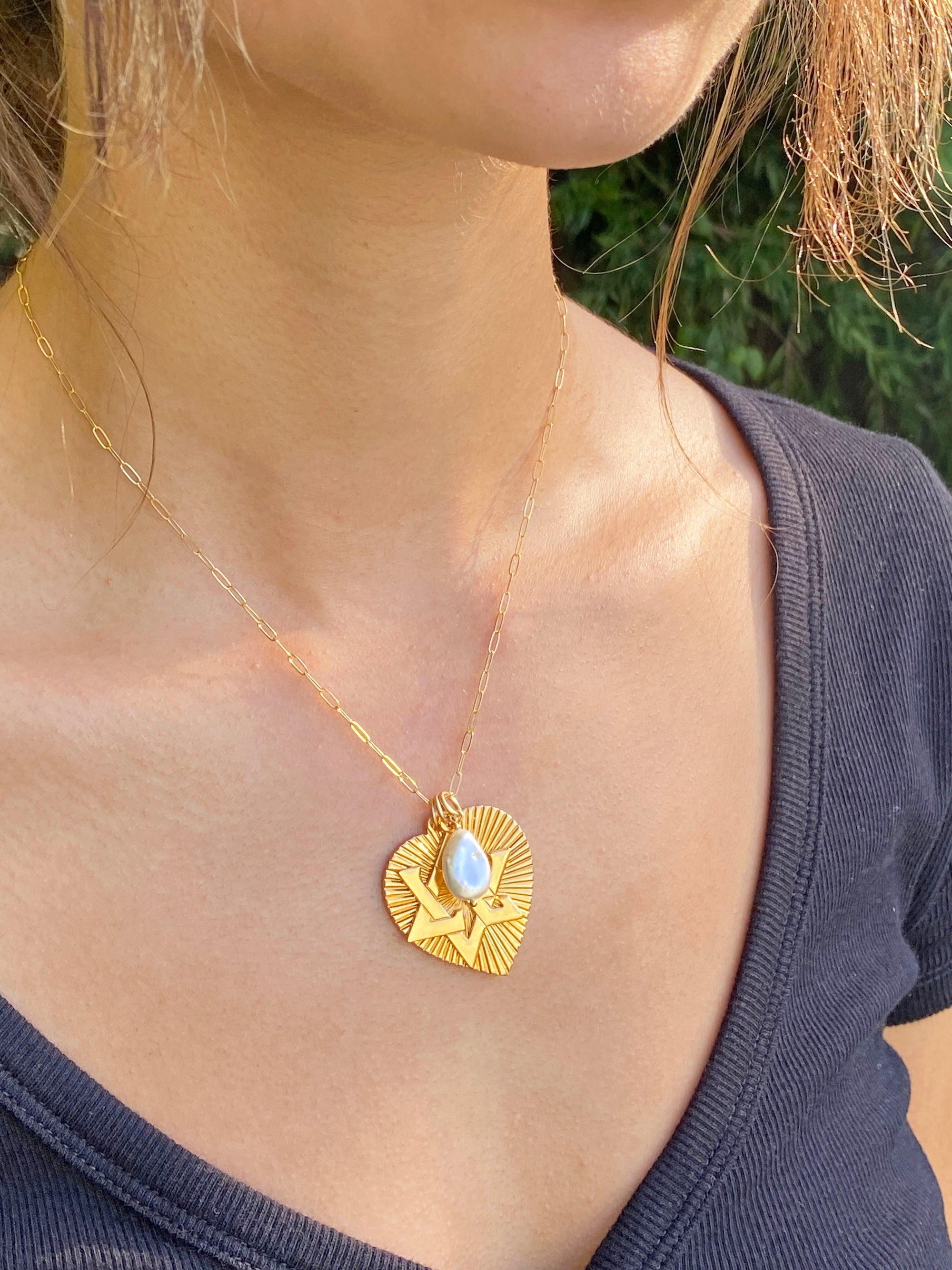 A gold ribbed heart pendant necklace with a Star of David design and moonstone accent on a paperclip chain, worn on a person's chest outdoors