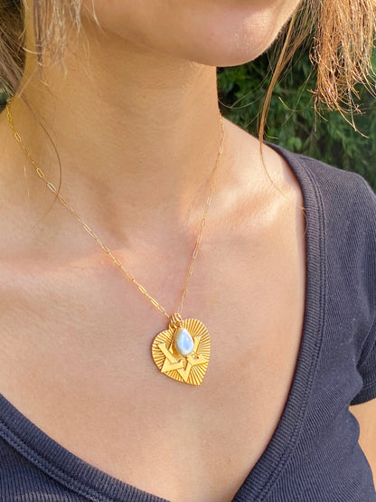 A gold ribbed heart pendant necklace with a Star of David design and moonstone accent on a paperclip chain, worn on a person's chest outdoors
