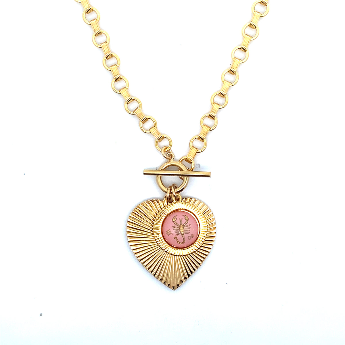 A gold ribbed heart-shaped pendant necklace with a Scorpio zodiac scorpion design in pink enamel center with toggle clasp closure on a gold round link chain against a white background