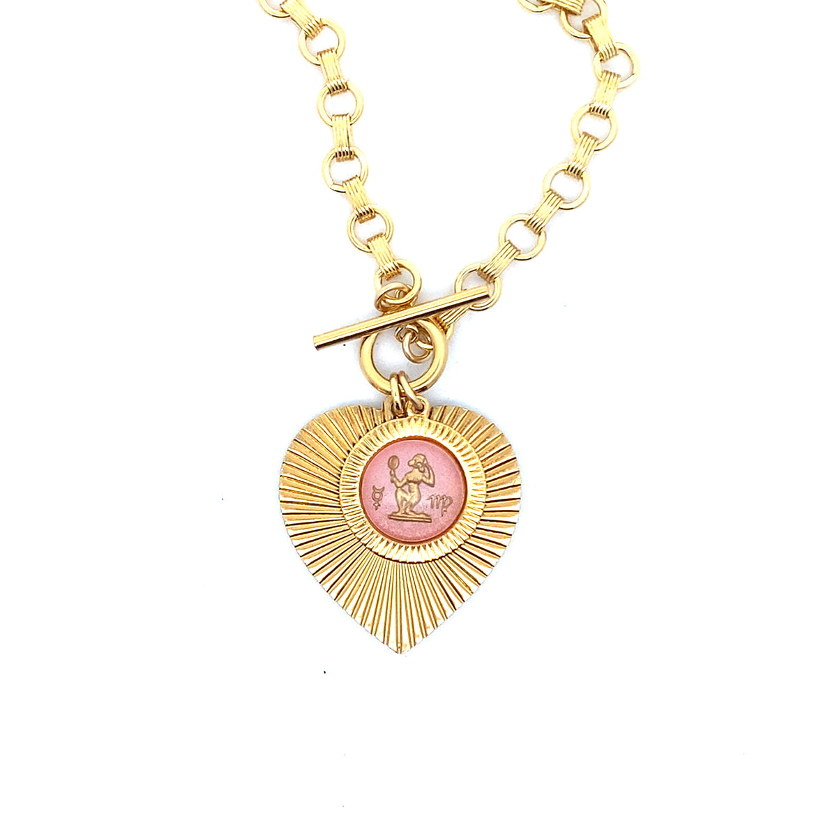 A gold ribbed heart-shaped pendant necklace with a Virgo zodiac maiden design in pink enamel center with toggle clasp closure on a gold round link chain against a white background