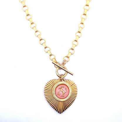 A gold ribbed heart-shaped pendant necklace with a Capricorn zodiac goat design in pink enamel center with toggle clasp closure on a gold round link chain against a white background