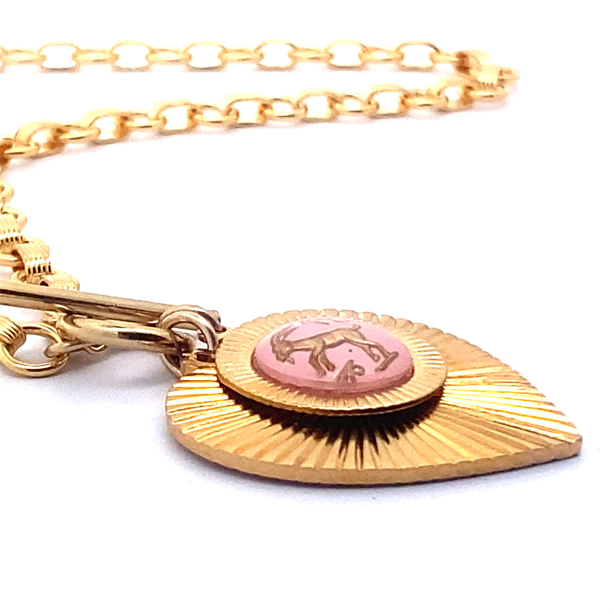 Close-up angled view of a gold ribbed heart-shaped pendant necklace with a Taurus zodiac bull design in pink enamel center with toggle clasp closure on a gold round link chain against a white background