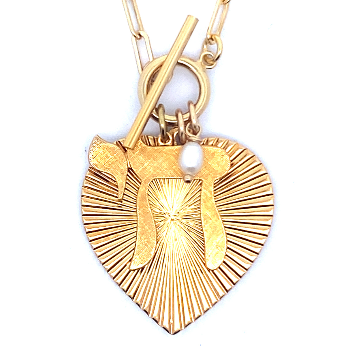 Close-up of the back of a gold ribbed heart-shaped pendant with starburst pattern and small pearl charm on a gold paperclip chain with toggle clasp against a white background