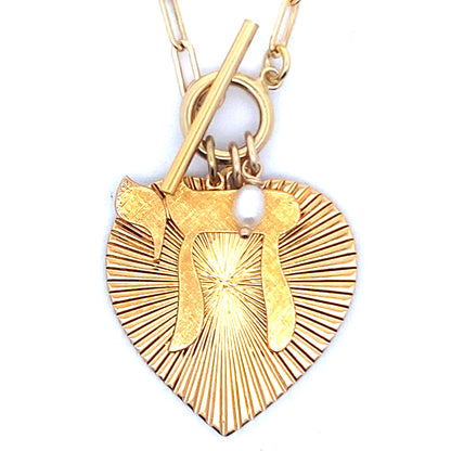Close-up of the back of a gold ribbed heart-shaped pendant with starburst pattern and small pearl charm on a gold paperclip chain with toggle clasp against a white background