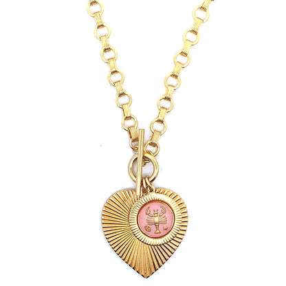 A gold ribbed heart-shaped pendant necklace with a Cancer zodiac crab design in pink enamel center with toggle clasp closure on a gold round link chain against a white background