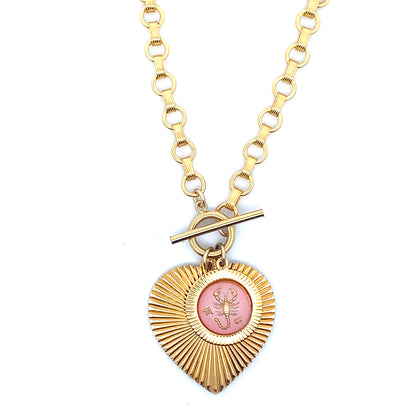 A gold ribbed heart-shaped pendant necklace with a Scorpio zodiac scorpion design in pink enamel center with toggle clasp closure on a gold round link chain against a white background