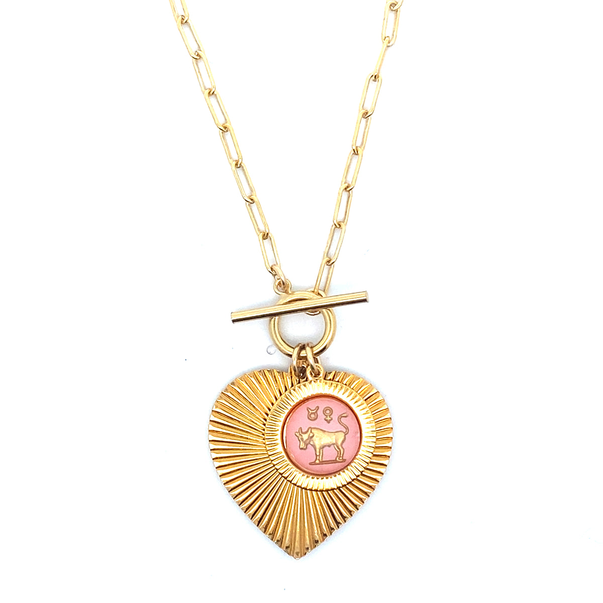 A gold ribbed heart-shaped pendant necklace with a Taurus zodiac bull design in pink enamel center with toggle clasp closure on a gold paperclip chain against a white background