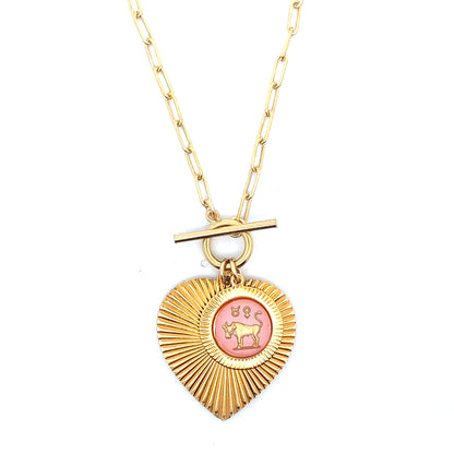 A gold ribbed heart-shaped pendant necklace with a Taurus zodiac bull design in pink enamel center with toggle clasp closure on a gold paperclip chain against a white background