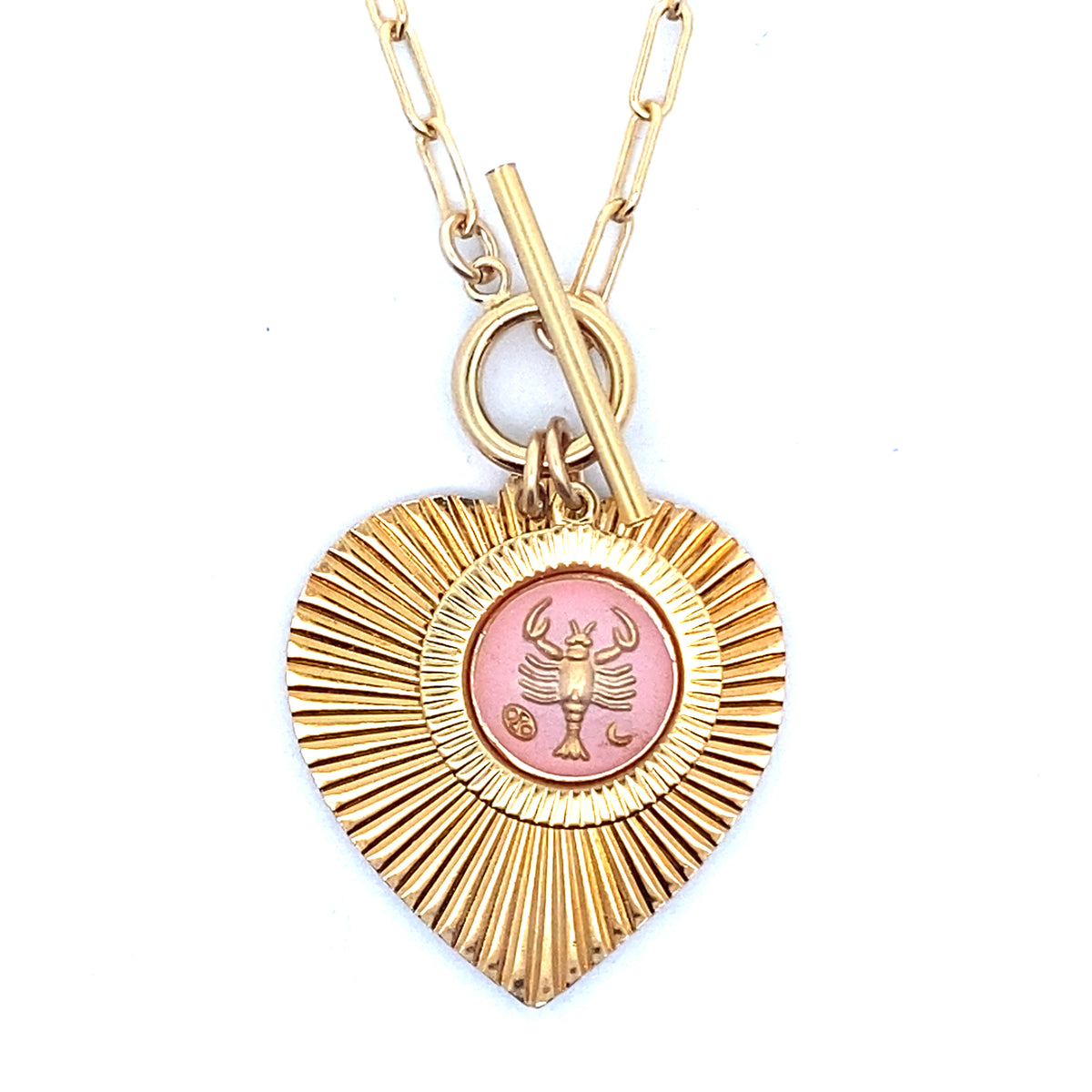 A gold ribbed heart-shaped pendant necklace with a Cancer zodiac crab design in pink enamel center with toggle clasp closure on a gold paperclip chain against a white background