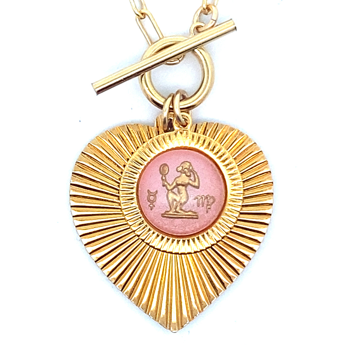 Close-up of a gold ribbed heart-shaped pendant necklace with a Virgo zodiac maiden design in pink enamel center with toggle clasp closure on a gold paperclip chain against a white background