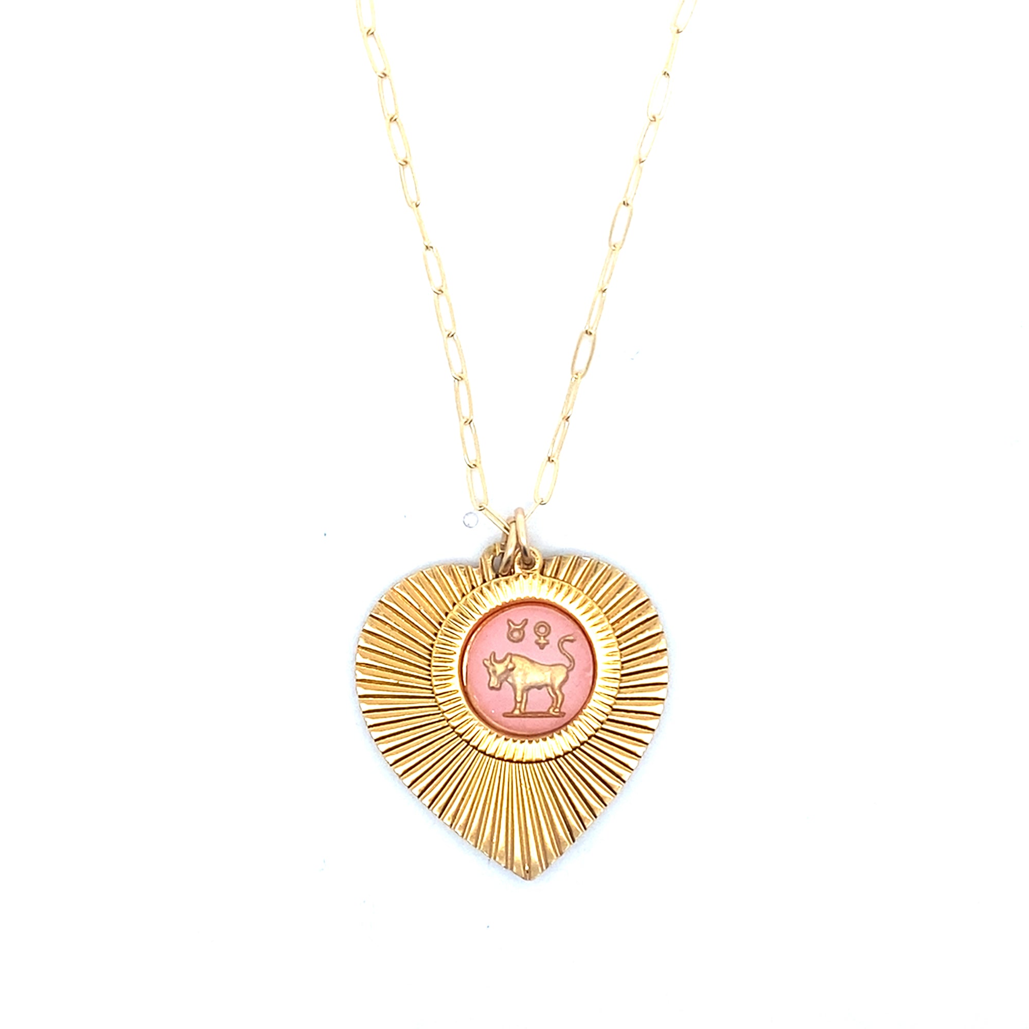 A gold ribbed heart-shaped pendant necklace with a Taurus zodiac bull design in pink enamel center on a gold paperclip chain against a white background