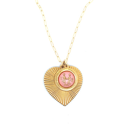 A gold ribbed heart-shaped pendant necklace with a Gemini zodiac twins design in pink enamel center on a gold paperclip chain against a white background