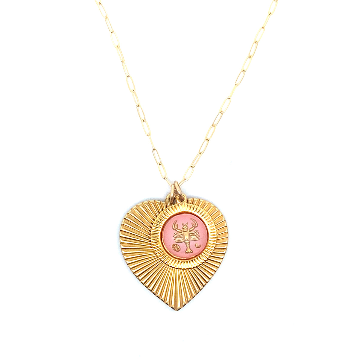 A gold ribbed heart-shaped pendant necklace with a Cancer zodiac crab design in pink enamel center on a gold paperclip chain against a white background