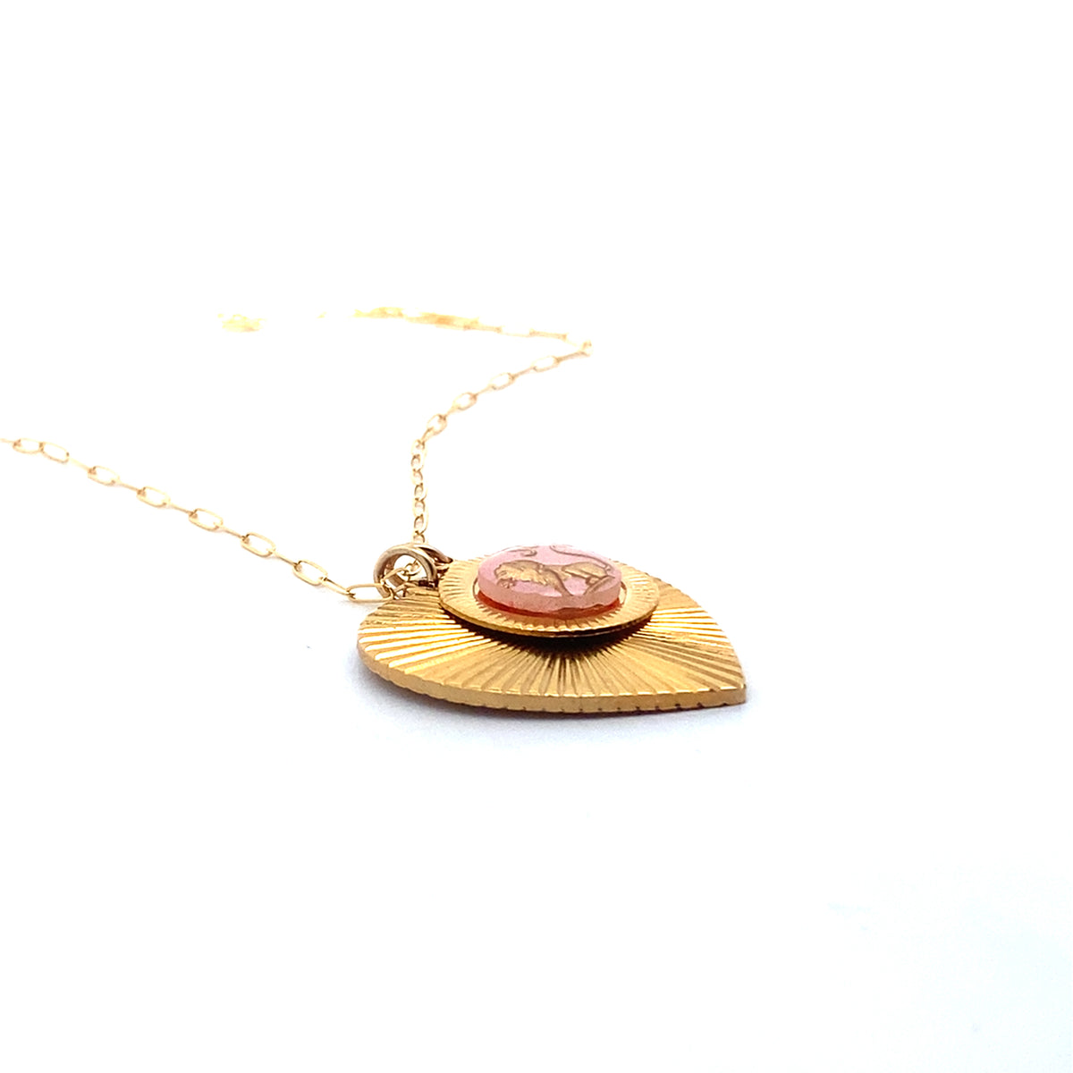 Angled side view of a gold ribbed heart-shaped pendant necklace with a Taurus zodiac bull design in pink enamel center on a gold paperclip chain against a white background