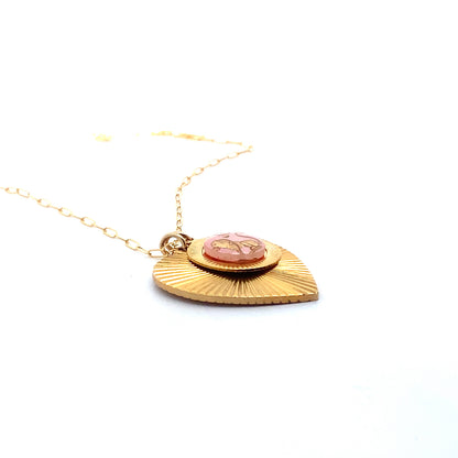 Angled side view of a gold ribbed heart-shaped pendant necklace with a Taurus zodiac bull design in pink enamel center on a gold paperclip chain against a white background