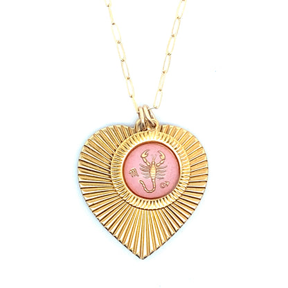 A gold ribbed heart-shaped pendant necklace with a Scorpio zodiac scorpion design in pink enamel center on a gold paperclip chain against a white background