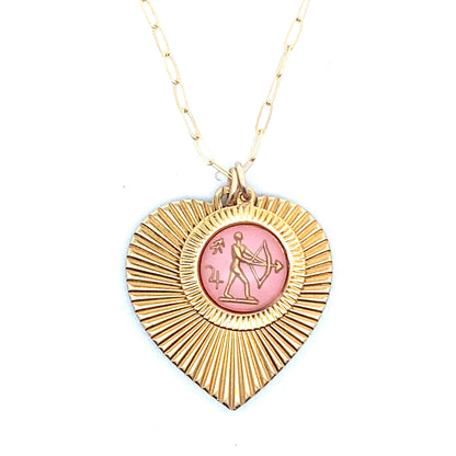 A gold ribbed heart-shaped pendant necklace with a Sagittarius zodiac archer design in pink enamel center on a gold paperclip chain against a white background