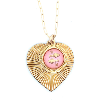 A gold ribbed heart-shaped pendant necklace with a Pisces zodiac fish design in pink enamel center on a gold paperclip chain against a white background
