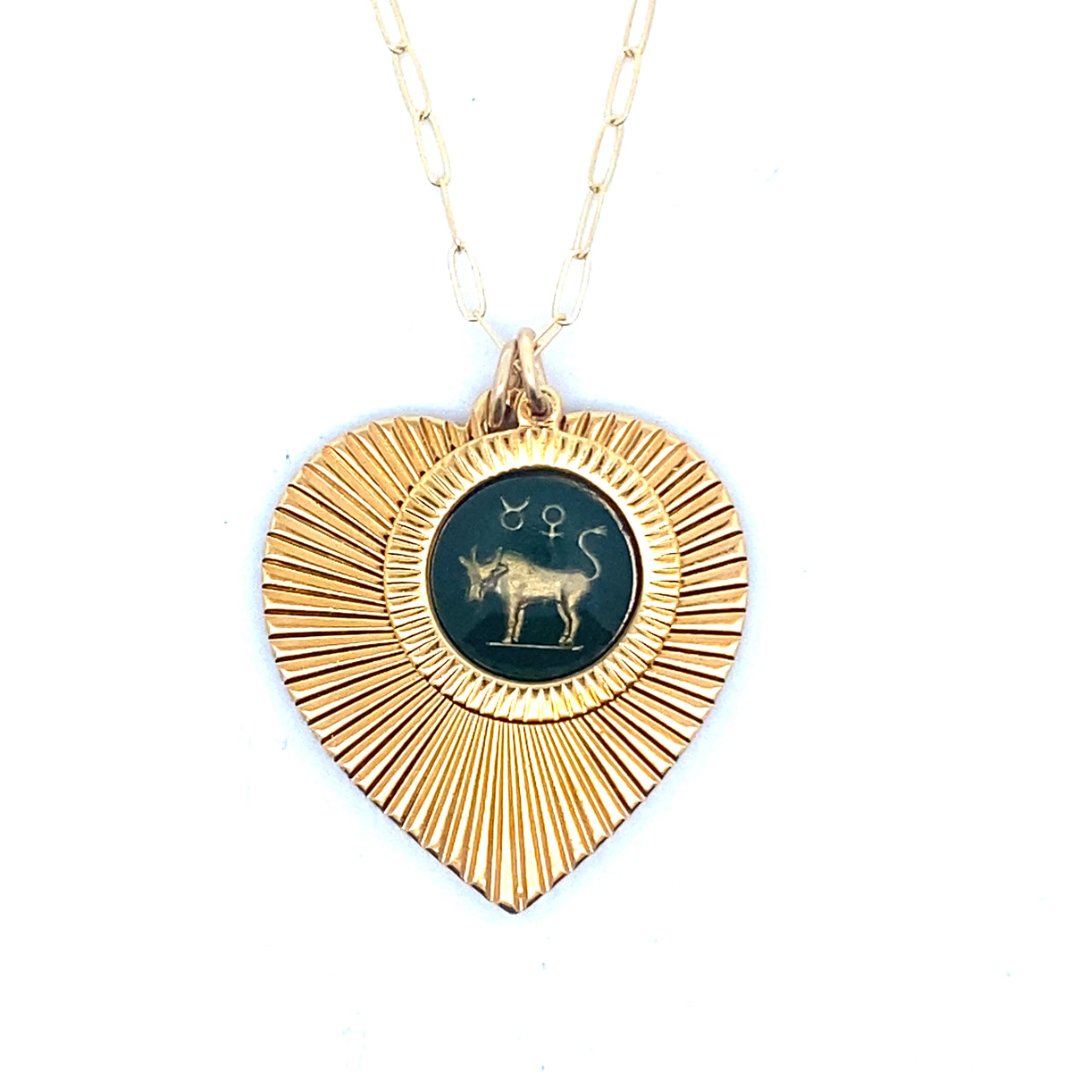 A gold ribbed heart-shaped pendant necklace with a Taurus zodiac bull design in dark teal enamel center on a gold paperclip chain against a white background